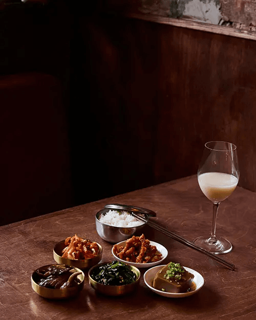 Table at Sunn’s NYC with assorted Korean banchan and a glass of makgeolli.